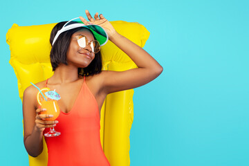 Pretty black lady in swimsuit lying on inflatable lilo and enjoying tropical cocktail over blue...