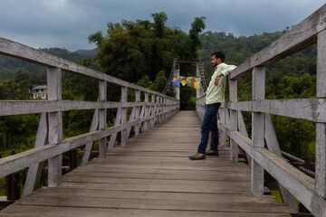 Man leaning on wooden bridge in himalayan greenery
