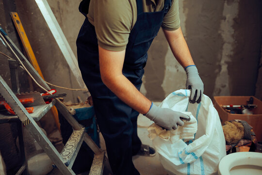 Construction Worker Collects Garbage in Trash Bag at the Working Site. Renovation worker cleaning up messy working space 