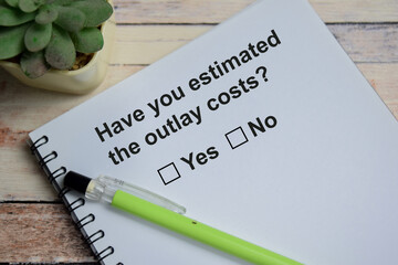 Have you estimated the outlay costs write on book isolated on Wooden Table. A person is answering question concept