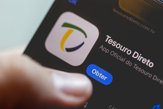 Tesouro Direto. Aplicativo oficial do Tesouro Direto na tela de um smartphone que um homem est&aacute; segurando em sua m&atilde;o. Investimento. Brasil. T&iacute;tulo P&uacute;blico.