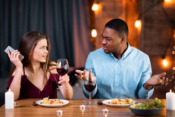 Annoyed Black Guy Arguing With His Girlfriend Busy With Cellphone On Date In Restaurant. Young Multiracial Couple Having Problems In Relationship During Romantic Dinner At Valentine's Day, Free Space