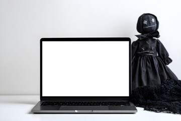 Laptop screen mockup on white desk with a black Halloween doll and minimal background.