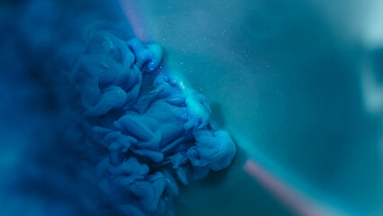 Ink splash. Mist art. Defocused blue green color sparkling liquid glitter rainbow texture spreading on abstract dark black background.