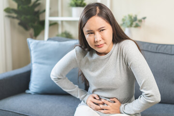 Sick asian young woman in pain, hand holding belly, stomach pain from food poisoning, girl hurt...