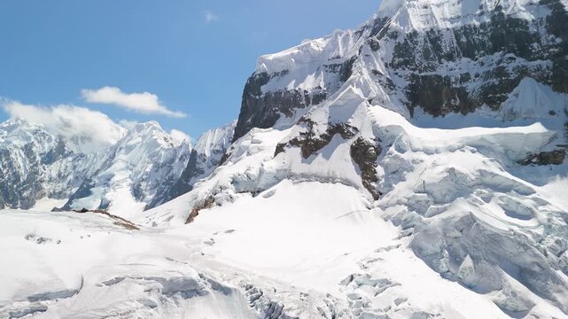 Aerial pan and tilt-up shot reveals the majestic, snow-covered summit of a rugged mountain from the Trapecio Pass on the famous Huayhuash trek in Peru.