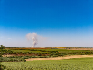 A large plume of smoke rises over a green field