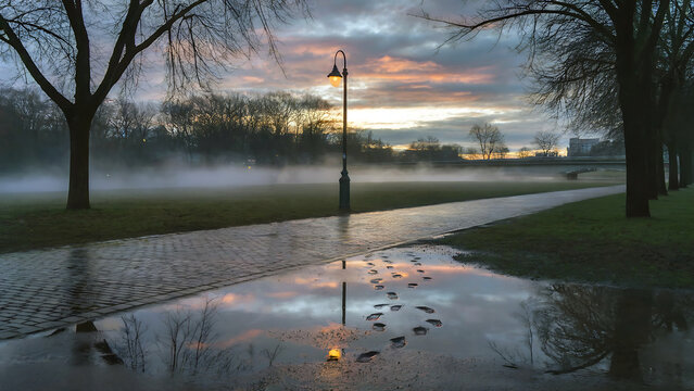 Footprints in puddle reflecting lamp and sunrise sky