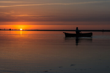 Fisherman in a Wooden fishing boat in calm river water, Old traditional boat, Silhouette man is fishing in a boat and rowing, Reflection of boat and paddle, sky sunset in Jijel a Algeria Africa.