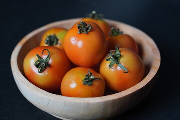 fresh tomatoes in a wooden bowl with dark background