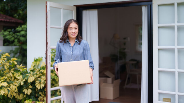 Adult Asian woman holds moving box new home entrance smiling homeowner moving day happy relocation residential property transition - Powered by Adobe