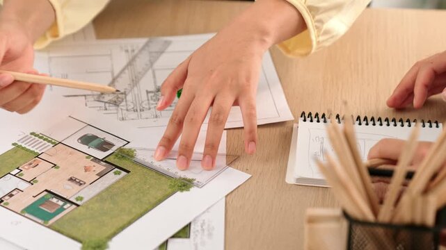 Architects using measurement tool and pencil tracing in building blueprint by coworker support on table with architectural document and wooden block scatter around at office. Closeup. Delineation.