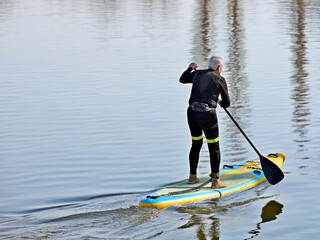 An elderly man swims in the water on a sports tourist inflatable spray with a paddle. Activity of people in old age. Modern water sports. Surfing with a paddle. Active recreation on the water