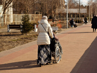 The guardian carries an elderly weak man in a wheelchair. Walk in the fresh air along the promenade on a sunny day. Caring for retirees and people in need of care. Life-long medicine. Joyful and activ