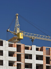 Two crane operators in overalls repair a high-rise tower crane working during the construction of a multi-storey building. Risky work at height. Lifting heavy building materials. City development