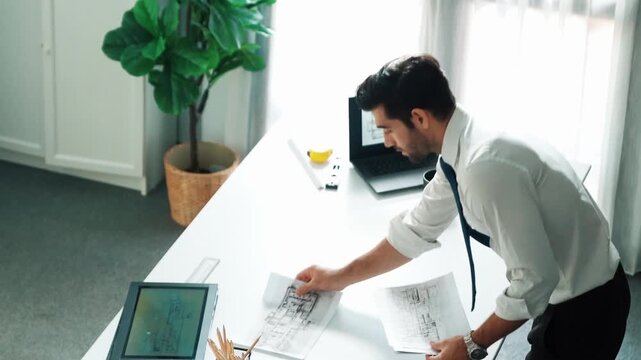 Architect engineer using laptop planning house design at office while sitting at meeting table with blueprint and equipment scatter around.Skilled civil engineer working at blueprint. Alimentation.