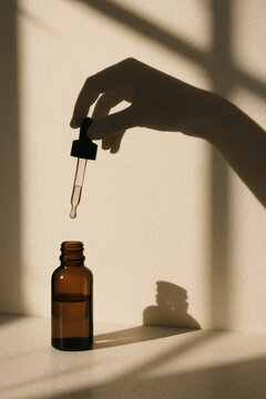 Dropper bottle with amber tint and hand shadow against a sunlit wall. For personal care, aromatherapy, and essential oil uses.