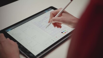 Over-the-shoulder shot of a person using a stylus to make notes and circle dates on a digital calendar app on a tablet. Concept of productivity, scheduling, and planning.