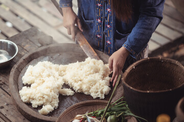 A woman's hands guide a wooden paddle through a bed of steaming sticky rice. This close-up captures the essential, hands-on process of preparing a staple food in rural Thailand.