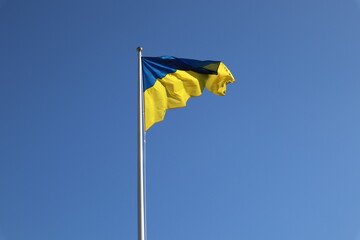 Photo of the flag of Ukraine. Blue and yellow flag against a blue sky. Blowing in the wind on a flagpole. Blue color from above, yellow from below. Chaotic folds. Ukraine. Stop the war in Ukraine.