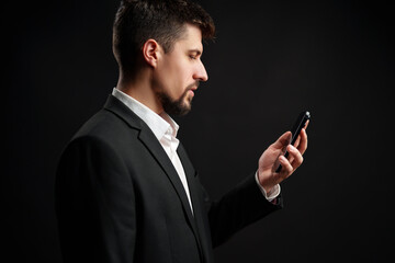Man in suit checks smartphone in a dark setting while preparing for an important event or meeting