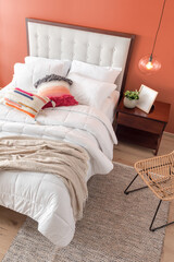 Tropical Summer-Styled Bedroom with Light Orange Walls, Bed with White Bedding, Lightweight Comforter, Beige Blanket, and Pillows, Complemented by a Wooden Nightstand and Flooring, top view.