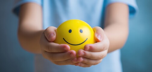 The joyful child holding a bright yellow smiley face ball in their hands.