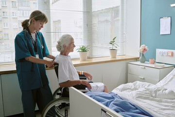 Young adult Caucasian female nurse assisting senior Caucasian woman sitting in wheelchair near...