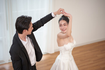 Asian couple having fun dancing together, groom twirls bride in white dress during wedding moment
