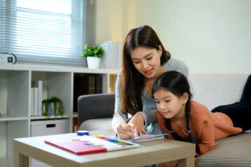 Loving mother helping daughter with homework or art project in a bright living room