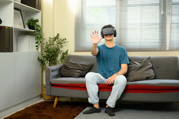 Obraz premium Young man wearing VR headset, experiencing virtual reality in a living room
