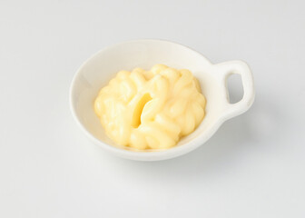 Small white ceramic bowl filled with creamy yellow mayonnaise, placed on clean white background, creating minimalistic and appetizing presentation