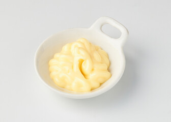 Small white ceramic bowl filled with creamy, smooth mayonnaise, placed on clean white background, showcasing its rich texture and pale yellow color