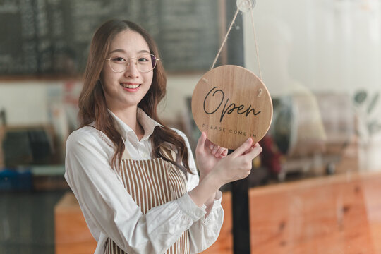 Cheerful shopkeeper welcomes customers by displaying open sign in a cozy storefront