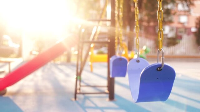 Empty children's playground at the park with swing swinging.