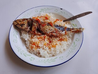 Top view of a simple Indonesian meal consisting of fried fish served with white rice and spicy chili sauce on a round enamel plate. Traditional homemade Asian cuisine