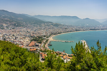 Naklejka premium Drone view of Alanya city, Turkey. Coastline, Mediterranean Sea, harbor, historic castle on the hill, and sprawling urban area with mountains in the background on a clear summer day. Alanya, Turkey