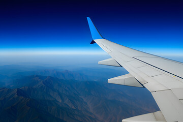Obraz premium Airplane Wing Flying High Above Majestic Mountain Range Under Clear Vibrant Blue Sky