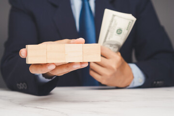 Businessman holding wooden blocks and dollar cash, symbolizing investment strategy and finance.