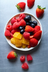 Top view mix fruit on the white plate raspberry, strawberry, blueberries and orange on light blue background