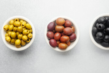 Variety of olives in bowls with wooden spoons on gray background, green olives, black and kalamata olives.
