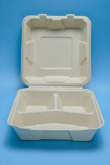 An open biodegradable food container with compartments, placed on a blue background. Ideal for sustainability, packaging, food delivery, or environmentally lifestyles