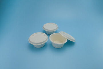 Three small white biodegradable food containers with lids, arranged on a blue background. Two containers are closed, and one is open lid. Perfect for sustainability, zero waste, plastic free