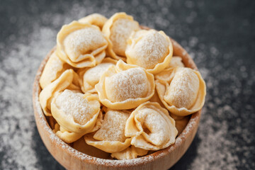 Wooden bowl filled with flour-dusted cappelletti pasta