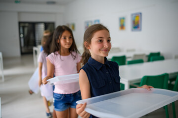 Kids in school canteen waiting for lunch, holding tray.