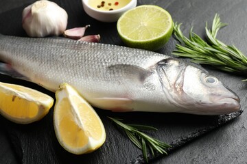 Fresh raw seabass with spices on black table, closeup. Fish and seafood delicacies