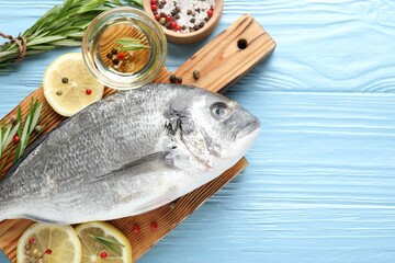 Fresh raw dourade fish with spices on blue wooden table, flat lay and space for text. Seafood delicacies