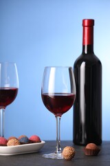 Delicious truffle bonbons and wine on black table against blue background