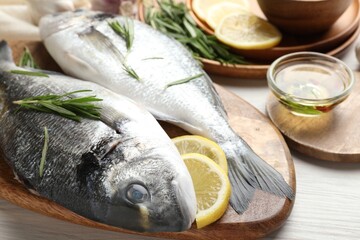 Fresh raw dorado fish, lemon slices, rosemary and spices on white wooden table, closeup. Organic...