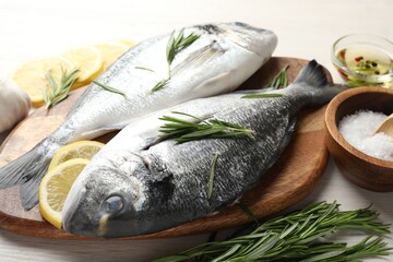 Fresh raw dorado fish, lemon slices, rosemary and spices on white wooden table, closeup. Organic seafood